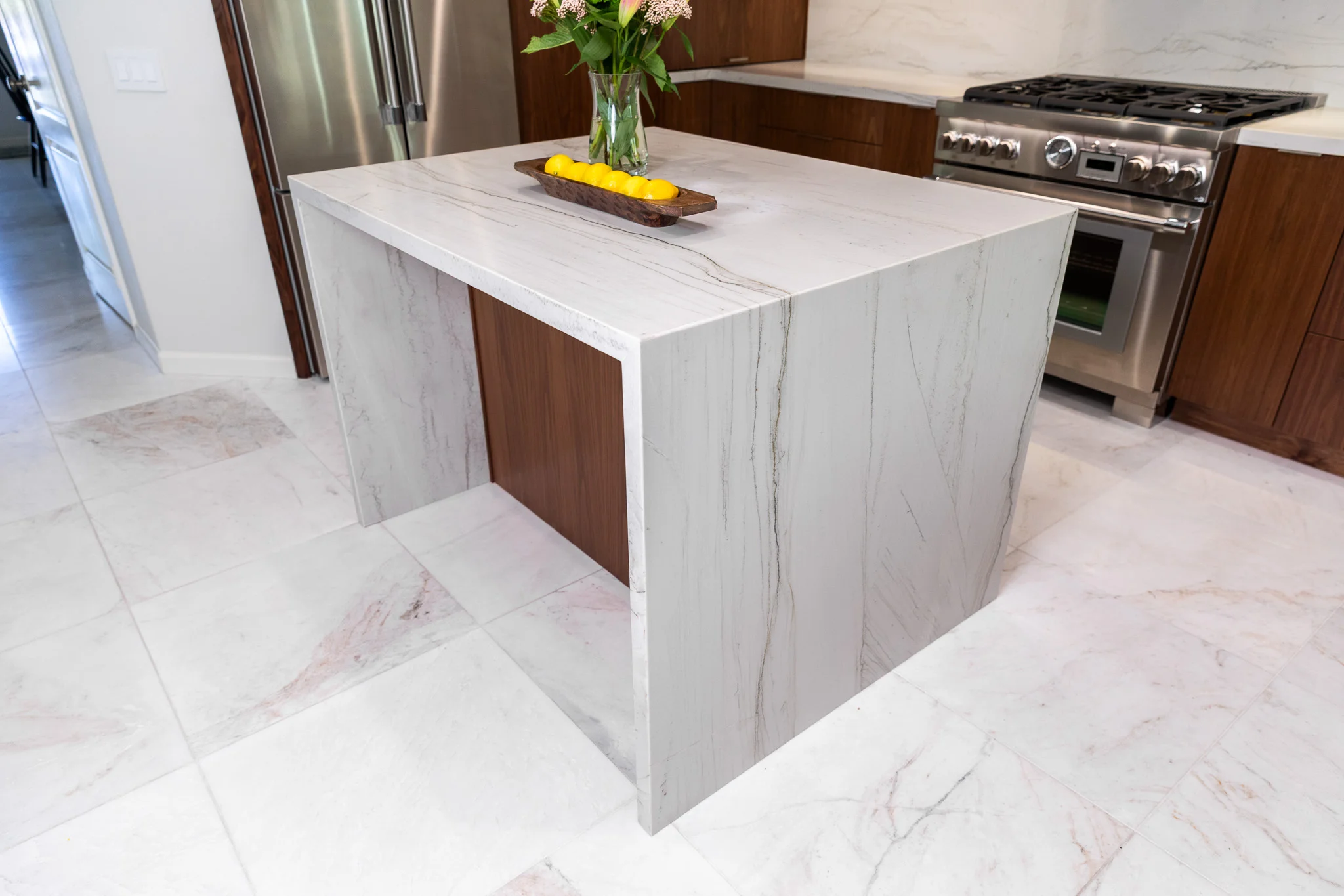 Modern kitchen island with white marble waterfall countertop and wood base cabinetry