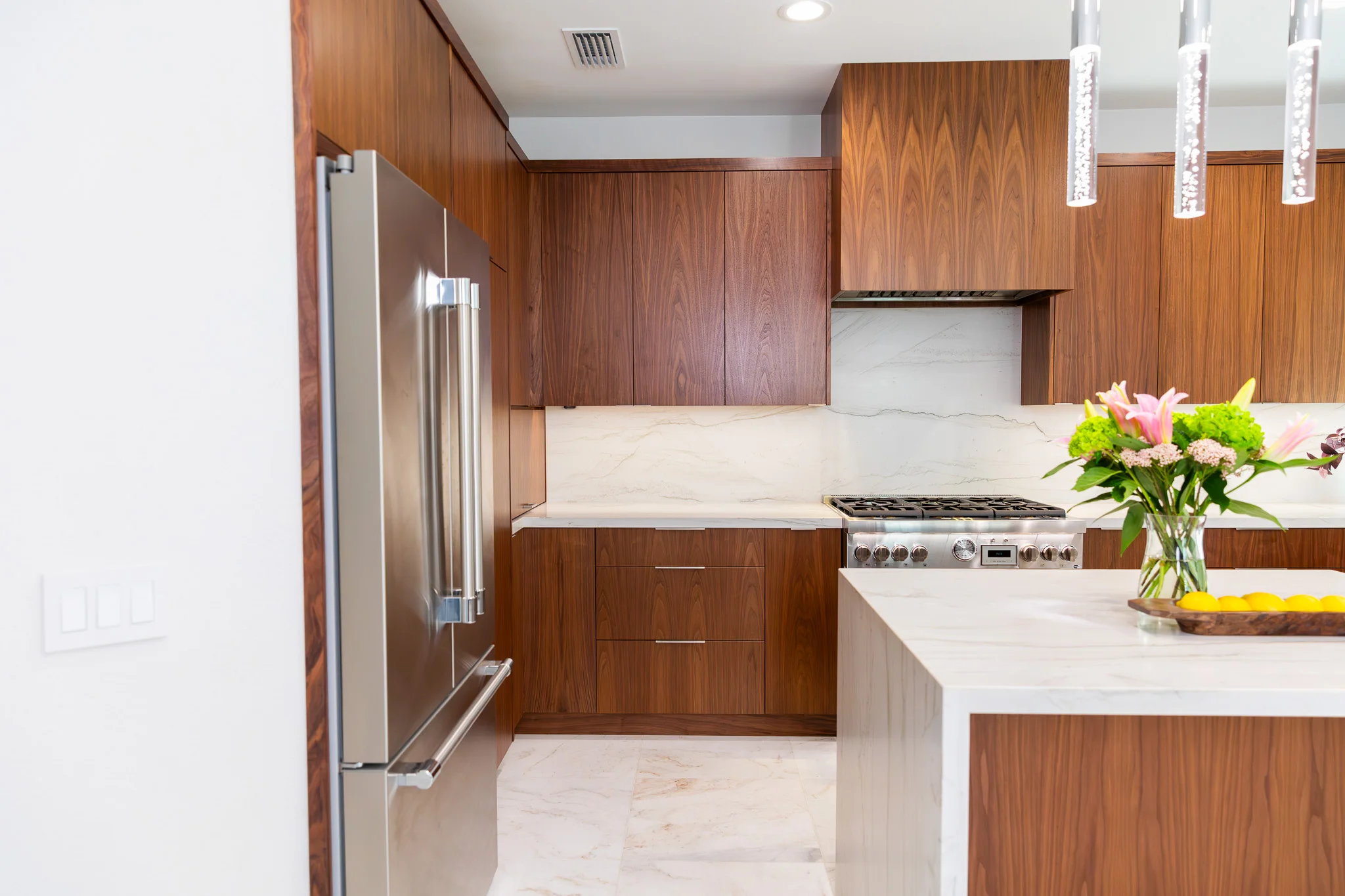 Modern kitchen with walnut cabinets, marble counters, stainless steel appliances, and island
